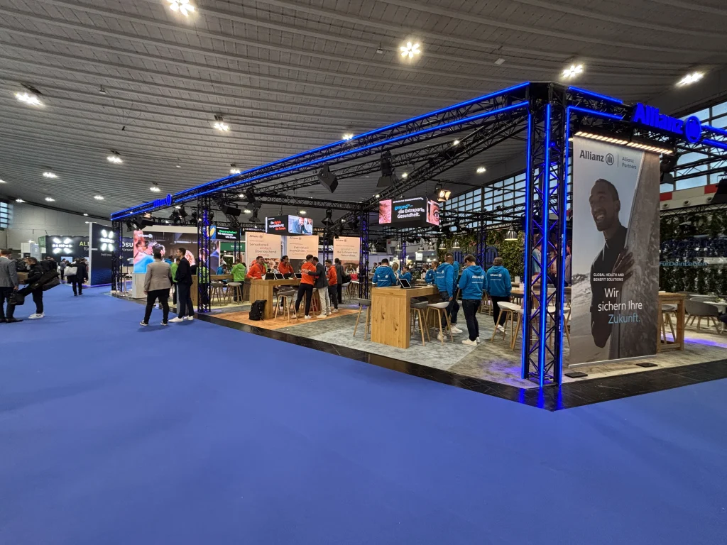 Allianz Stand auf einer Messe mit Besuchern und Werbeplakaten im Hintergrund.