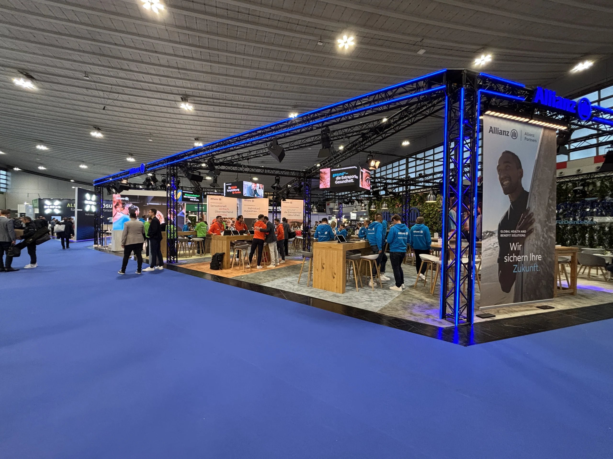 Allianz Stand auf einer Messe mit Besuchern und großem Werbebanner im Hintergrund.