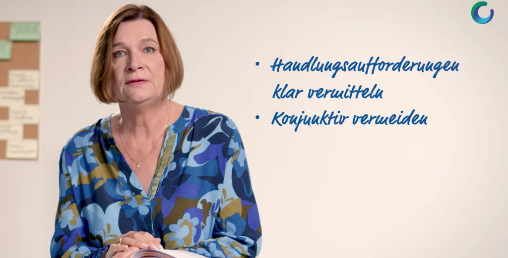 Eine Frau spricht vor einer hellen Wand mit Stichpunkten über klare Kommunikation.